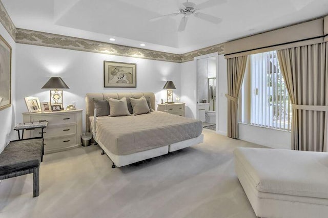 bedroom featuring light carpet, ensuite bath, a raised ceiling, and a ceiling fan