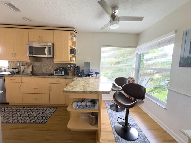 kitchen featuring open shelves, light brown cabinetry, a peninsula, and stainless steel appliances