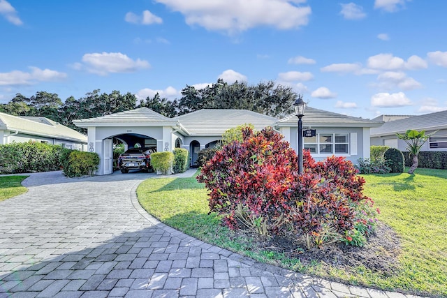 view of front of house with a tiled roof, decorative driveway, stucco siding, a carport, and a front lawn