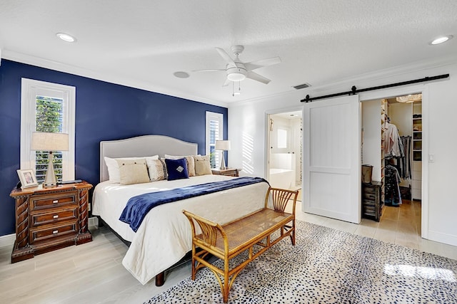 bedroom featuring visible vents, a spacious closet, a barn door, ornamental molding, and a textured ceiling