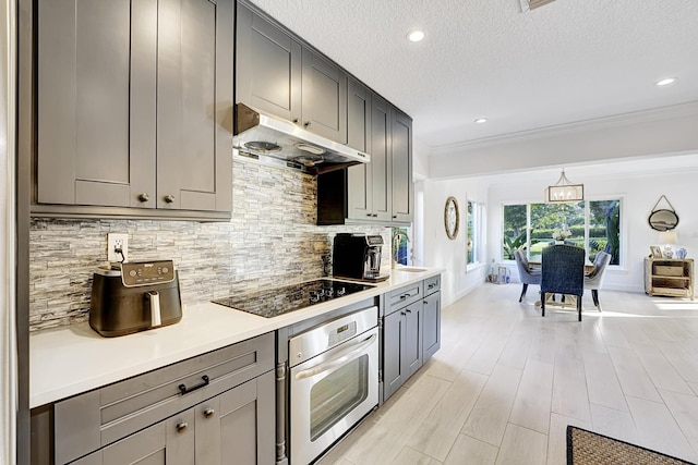 kitchen featuring decorative backsplash, oven, light countertops, black electric cooktop, and under cabinet range hood