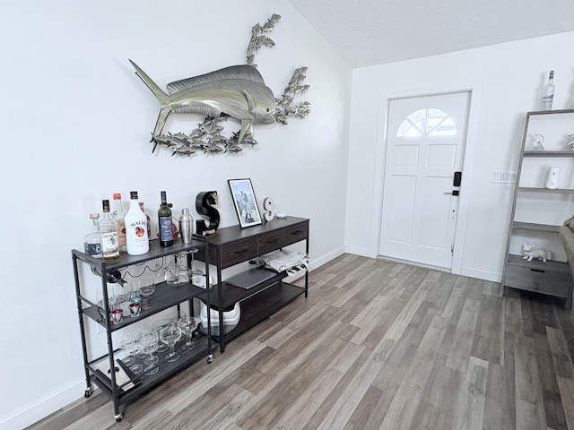 foyer entrance with a textured ceiling, baseboards, and wood finished floors