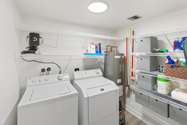 clothes washing area with visible vents, washing machine and dryer, electric water heater, wood finished floors, and laundry area