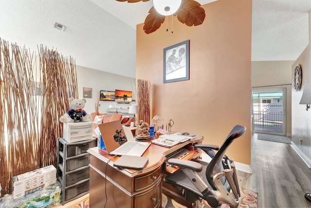 office with baseboards, visible vents, lofted ceiling, wood finished floors, and a textured ceiling