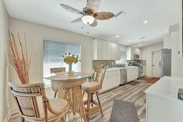 kitchen featuring stainless steel appliances, white cabinets, backsplash, and light wood finished floors