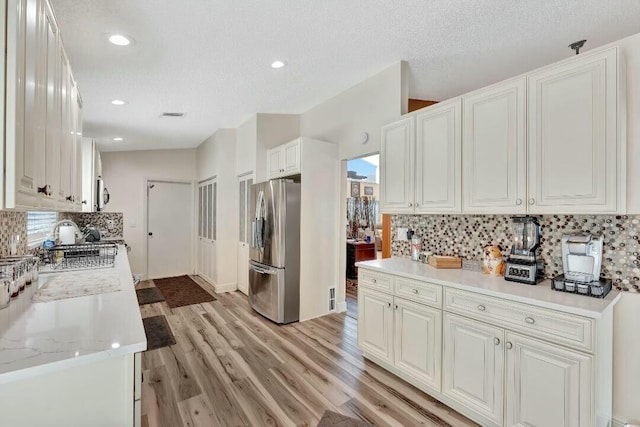 kitchen featuring light wood finished floors, light countertops, white cabinetry, stainless steel refrigerator with ice dispenser, and backsplash