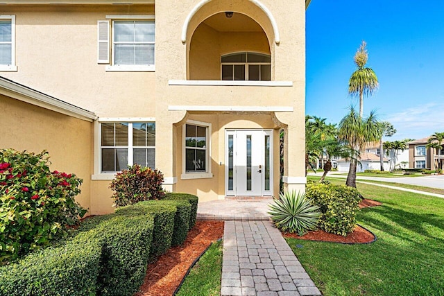 property entrance featuring a balcony, a yard, and stucco siding