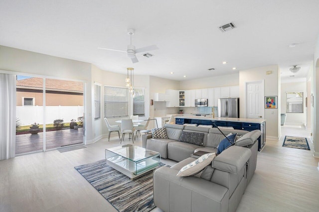 living room featuring ceiling fan, visible vents, baseboards, and light wood-style flooring