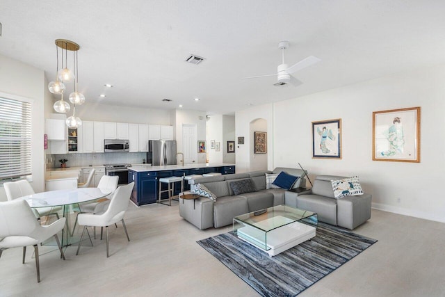 living area featuring a ceiling fan, baseboards, visible vents, arched walkways, and light wood-type flooring