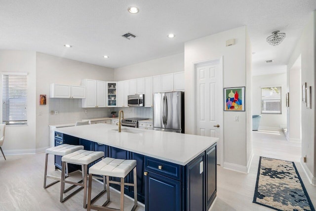 kitchen with a center island with sink, visible vents, blue cabinetry, stainless steel appliances, and white cabinetry