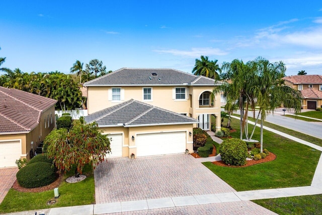 traditional home with stucco siding, a tile roof, decorative driveway, a front yard, and an attached garage