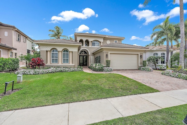 mediterranean / spanish house featuring decorative driveway, a tile roof, stucco siding, an attached garage, and a front lawn