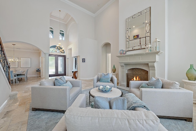 living room with a warm lit fireplace, stone tile floors, baseboards, crown molding, and a notable chandelier