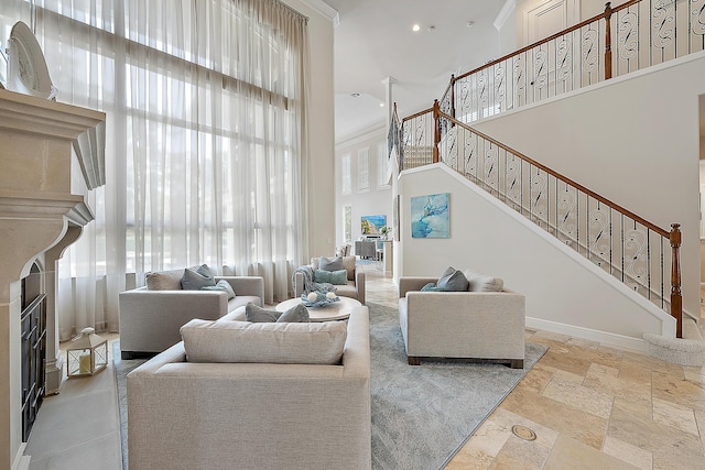 living area featuring stone tile floors, baseboards, a fireplace with raised hearth, stairway, and a high ceiling