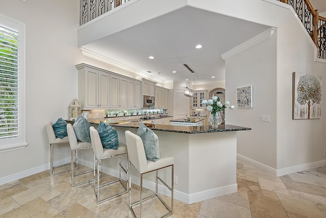 kitchen with a breakfast bar area, stone tile floors, stainless steel microwave, dark stone counters, and baseboards