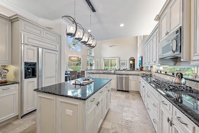 kitchen featuring stone tile floors, stainless steel appliances, a peninsula, a kitchen island, and dark stone countertops