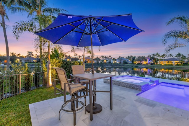 pool at dusk featuring a patio area, fence, outdoor dining area, and an in ground hot tub