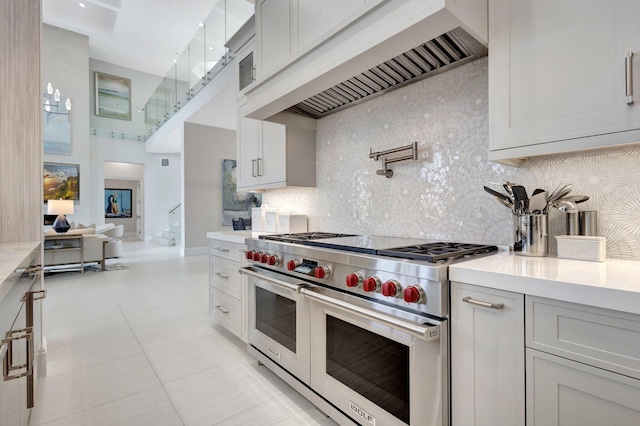 kitchen featuring range with two ovens, light countertops, custom range hood, backsplash, and light tile patterned flooring