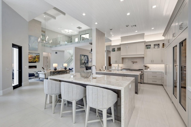 kitchen featuring a spacious island, glass insert cabinets, backsplash, a kitchen bar, and a sink