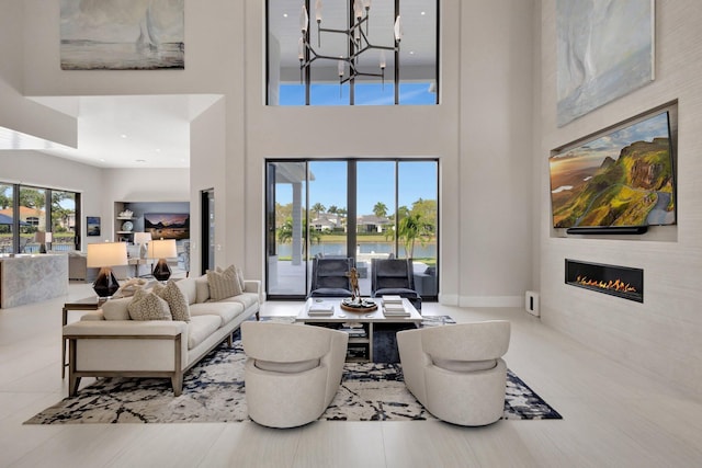 living room with a glass covered fireplace, baseboards, a high ceiling, and an inviting chandelier