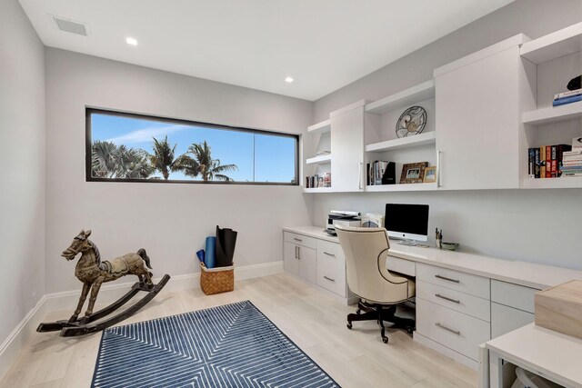 office space with baseboards, built in desk, visible vents, and light wood-style floors