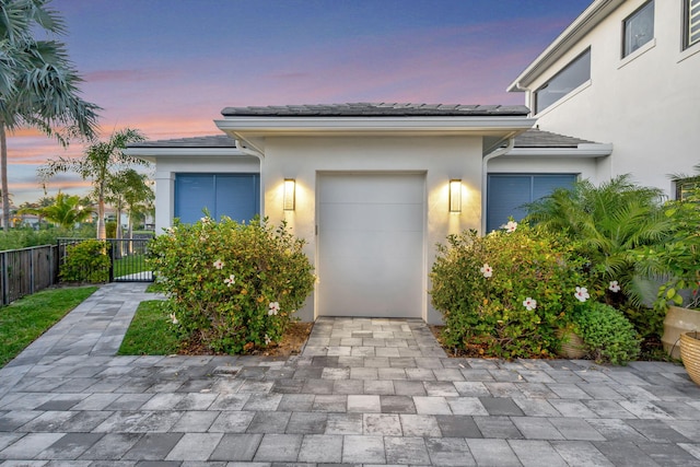 view of front of house with a garage, decorative driveway, fence, and stucco siding