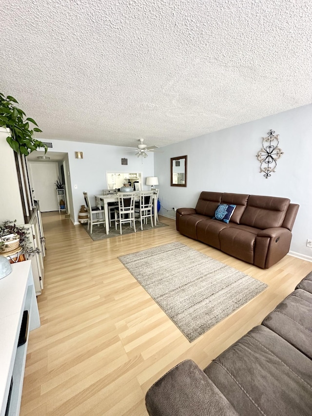 living room featuring baseboards, ceiling fan, light wood-style flooring, and a textured ceiling