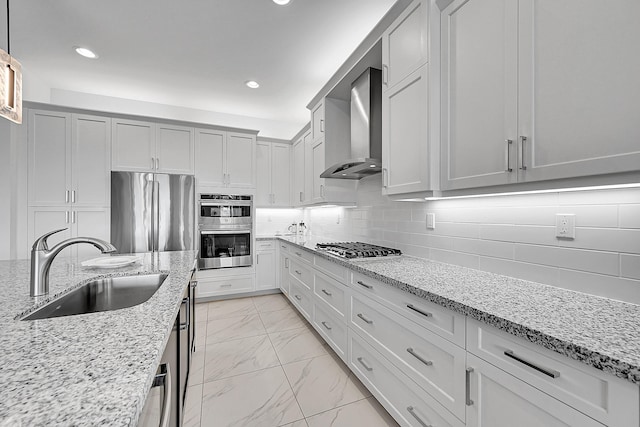 kitchen featuring marble finish floor, stainless steel appliances, backsplash, a sink, and wall chimney exhaust hood