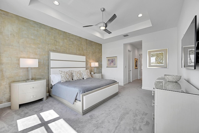 bedroom with a ceiling fan, a tray ceiling, light carpet, and baseboards