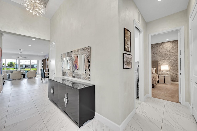 corridor featuring marble finish floor, visible vents, a high ceiling, an inviting chandelier, and baseboards