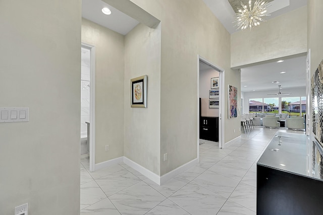 hallway with a chandelier, recessed lighting, marble finish floor, and baseboards