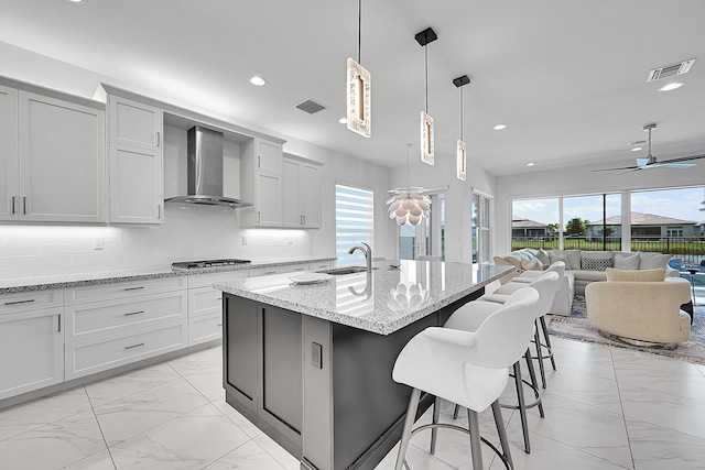 kitchen featuring marble finish floor, wall chimney exhaust hood, a sink, and visible vents