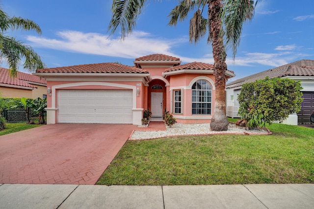 mediterranean / spanish house featuring an attached garage, a tile roof, decorative driveway, stucco siding, and a front lawn