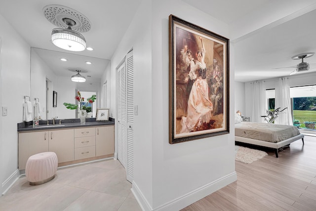 corridor featuring light wood finished floors, recessed lighting, a sink, and baseboards