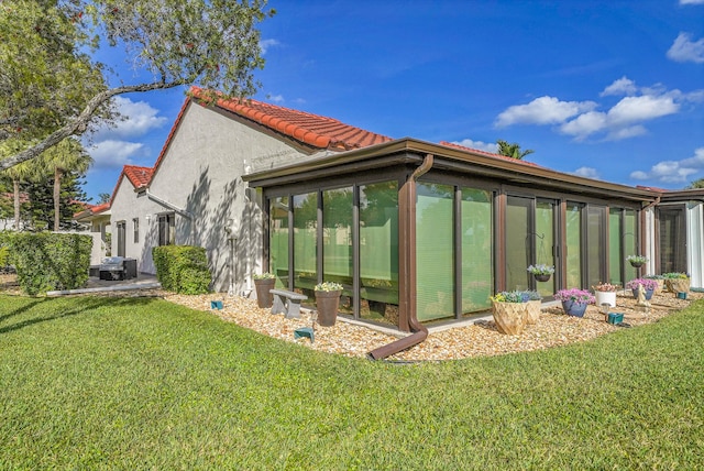 exterior space featuring a sunroom, a tile roof, a lawn, and stucco siding