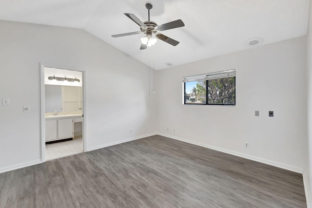 unfurnished bedroom with lofted ceiling, a sink, wood finished floors, baseboards, and ensuite bath