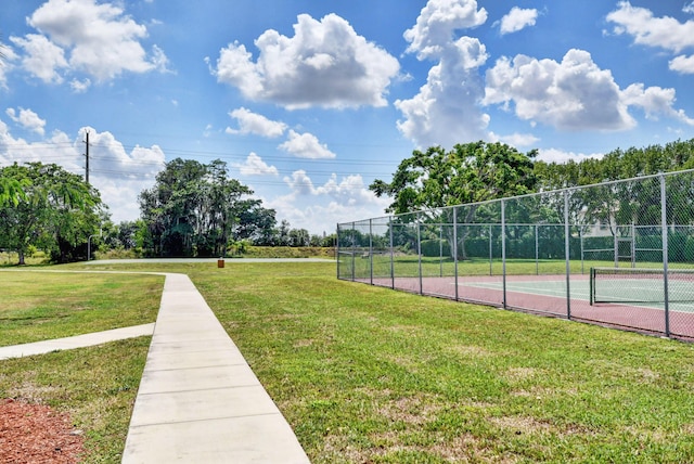 view of property's community with a tennis court, a yard, and fence