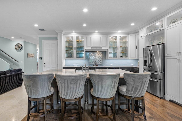 kitchen featuring white cabinetry, visible vents, stainless steel fridge with ice dispenser, tasteful backsplash, and a center island with sink