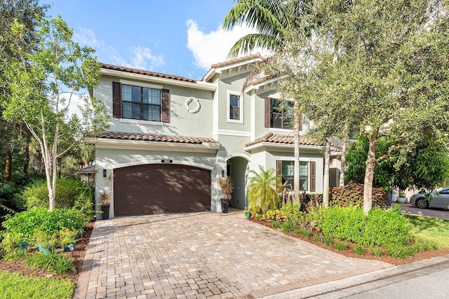 mediterranean / spanish house with decorative driveway, an attached garage, a tile roof, and stucco siding