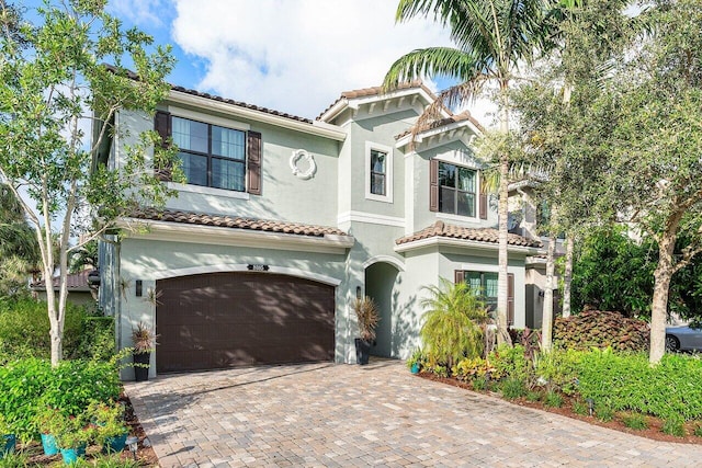 mediterranean / spanish-style house featuring a garage, a tile roof, decorative driveway, and stucco siding