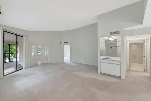 unfurnished living room with visible vents, light carpet, french doors, high vaulted ceiling, and a sink