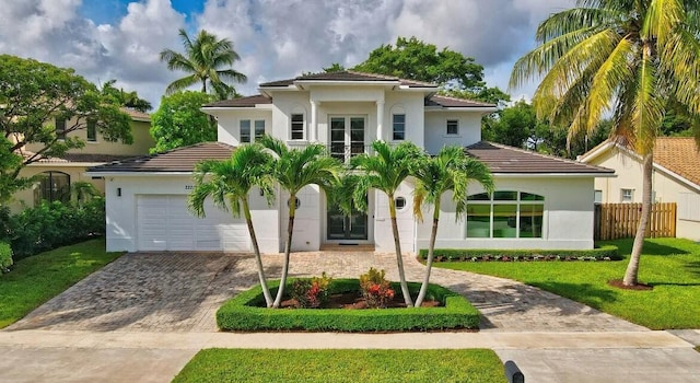 mediterranean / spanish house with a garage, fence, decorative driveway, a front yard, and stucco siding