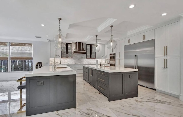 kitchen with a sink, light countertops, appliances with stainless steel finishes, a center island with sink, and custom range hood