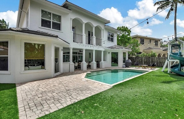 rear view of house with a lawn, a patio, a balcony, fence, and stucco siding