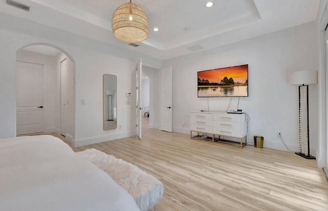 bedroom featuring visible vents, arched walkways, a raised ceiling, light wood-style flooring, and recessed lighting