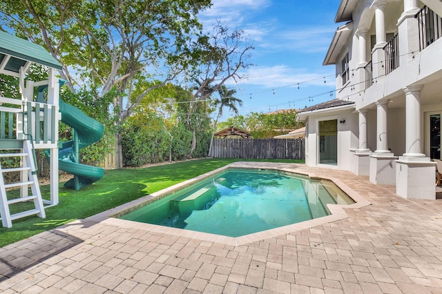 view of swimming pool featuring a patio, a playground, a fenced backyard, a lawn, and a fenced in pool