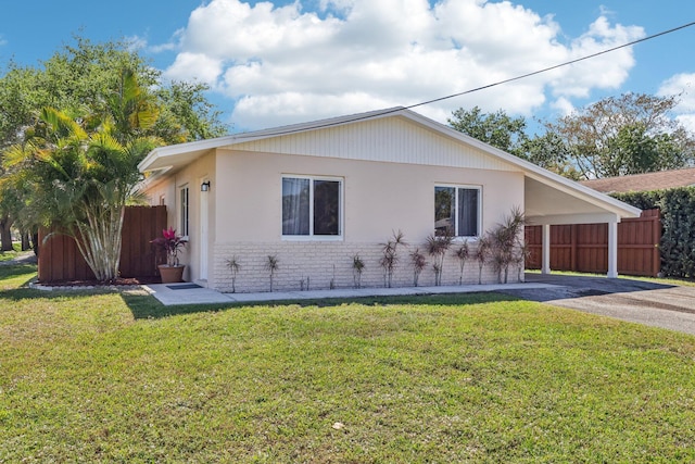 view of side of home featuring brick siding, a yard, fence, a carport, and driveway