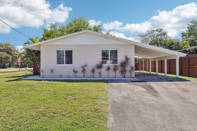 view of front of property featuring brick siding, an attached carport, a front lawn, fence, and aphalt driveway