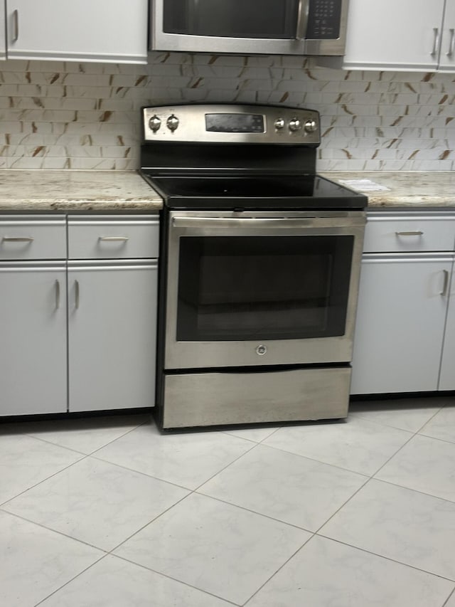 kitchen featuring stainless steel appliances, gray cabinets, light tile patterned flooring, and tasteful backsplash