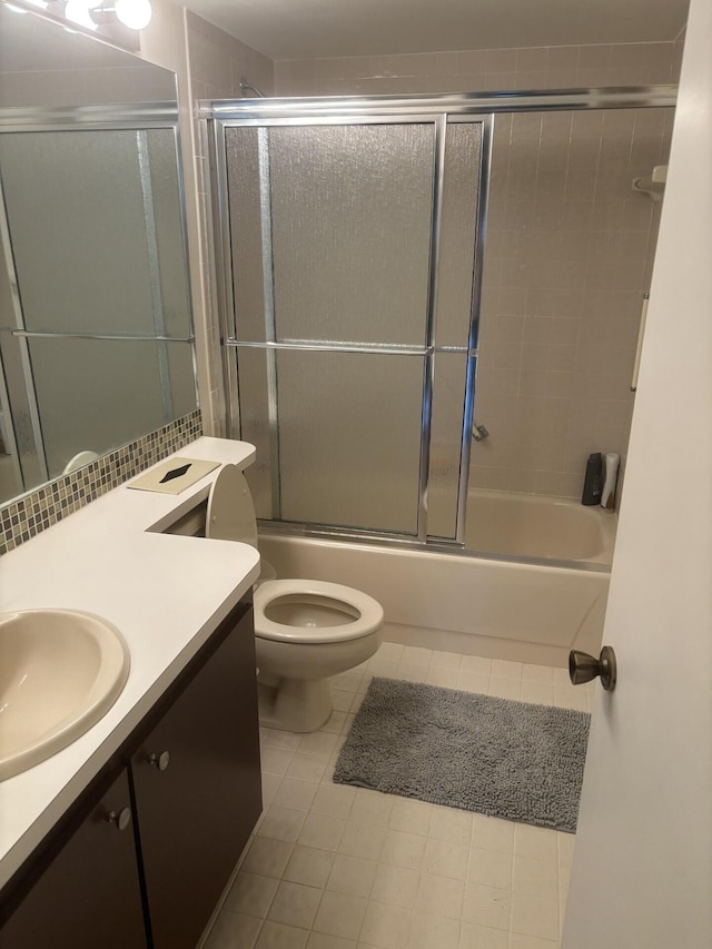 bathroom featuring toilet, bath / shower combo with glass door, vanity, and tile patterned floors